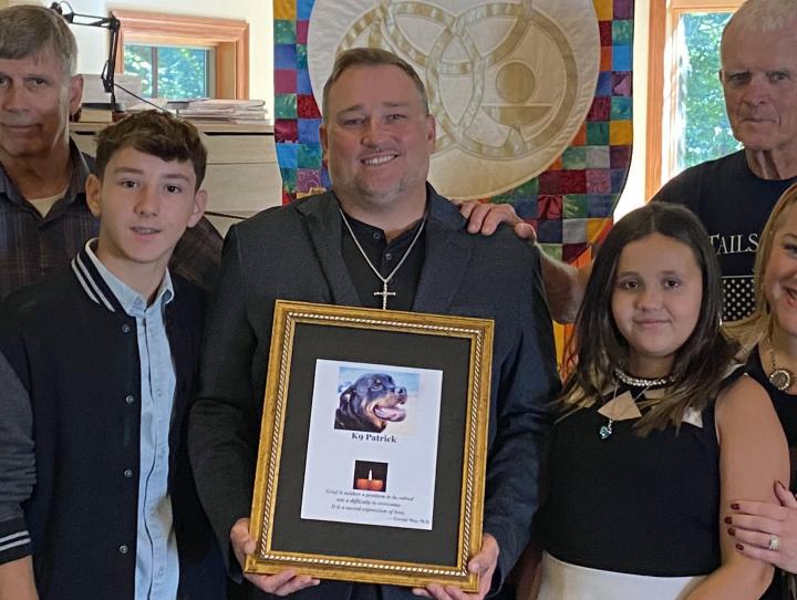 David Kist, surrounded by his son, daughter, and wife, holds a photo of his service dog, Patrick. At left is Linda Blick, President and Founding Board of Trustees Member, Tails of Hope Foundation, and her husband; at right in the back is Kevin Henry, a Veteran and a Tails of Hope Foundation Contributor and Volunteer.
