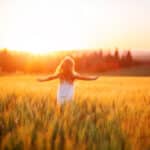 Little girl in white dress in field at sunset