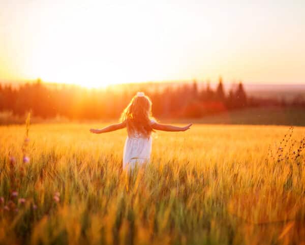 Little girl in white dress in field at sunset
